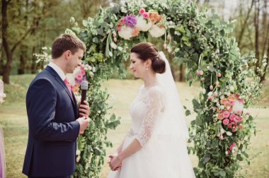 İlkbaharda klasik düğün. Tören. Damat söz veriyor ve yüzüğü elinde tutuyor..