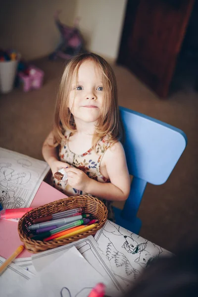 A girl with fair hair draws with felt-tip pens in the children\'s room at the table.