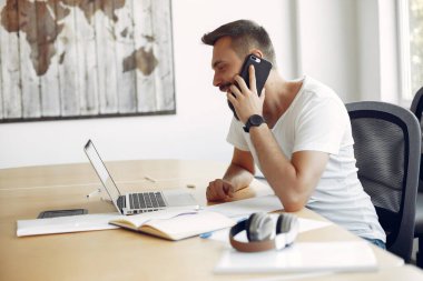 Genç öğrenci masada oturuyor ve dizüstü bilgisayarını kullanıyor.