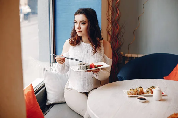 Женщина сидит за столом и ест суши в кафе — стоковое фото