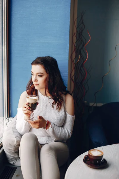 Meisje in een witte trui zit alleen in cafe — Stockfoto