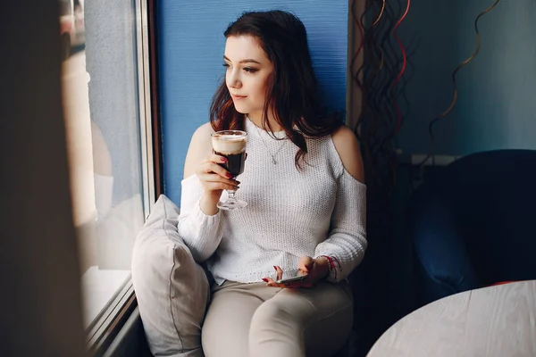 Girl in a white sweater sitting alone in cafe — Stock Photo, Image