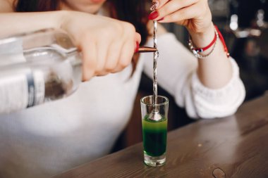 Beyaz kazaklı bir kadın cama yeşil şurup döküyor.