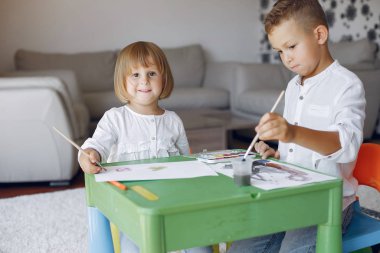 Çocuklar yeşil masada oturuyor ve resim çiziyor.