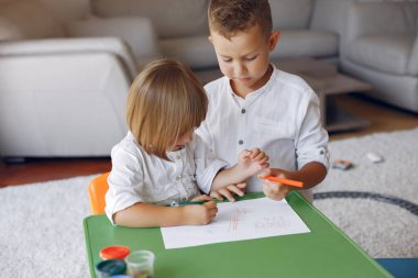 Çocuklar yeşil masada oturuyor ve resim çiziyor.