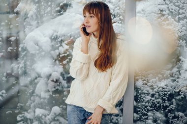 Evdeki geniş pencerenin yanında duran kadın.