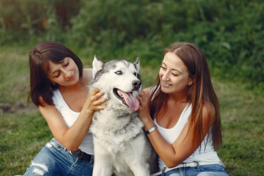 Bir bahar parkında iki kız sevimli bir köpekle oynuyor.