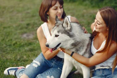 Bir bahar parkında iki kız sevimli bir köpekle oynuyor.