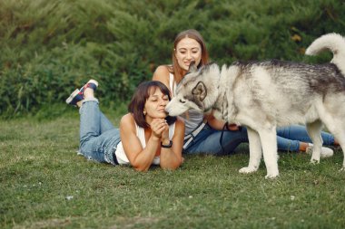 Bir bahar parkında iki kız sevimli bir köpekle oynuyor.