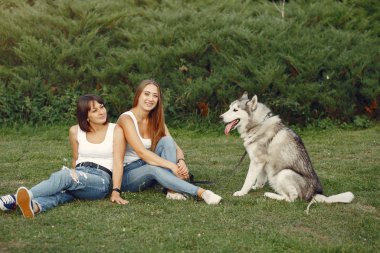 Bir bahar parkında iki kız sevimli bir köpekle oynuyor.