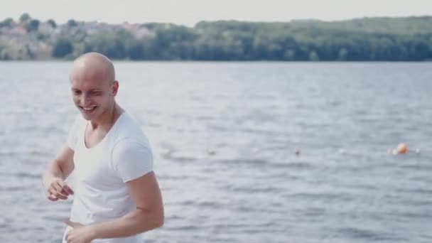 Retrato de hombre calvo en camiseta blanca bailando cerca del lago — Vídeos de Stock