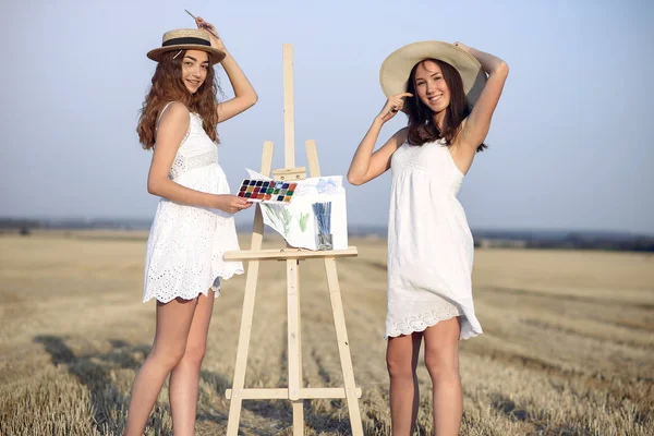 Two girls in a white dress painting in a field — Stock Photo, Image