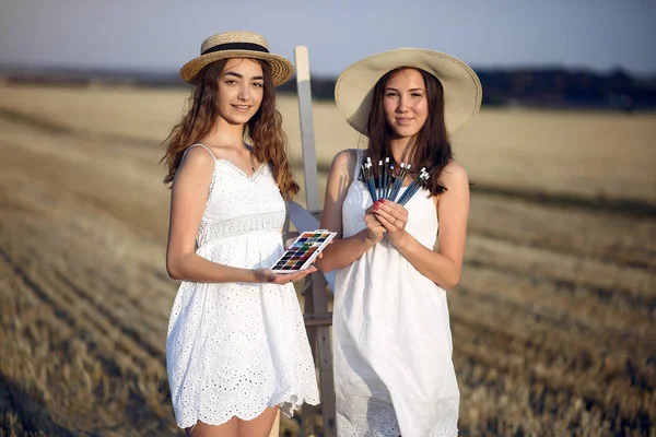 Dwie dziewczyny w białej sukience malują na polu — Zdjęcie stockowe