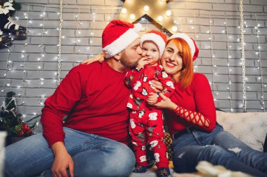 Noel süslemeleriyle evde bir yatakta oturan aile.