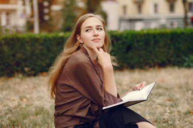 Parkta çalışan sevimli bir öğrenci ve not defterini kullanıyor.