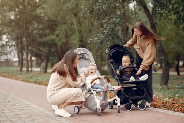 Sonbahar parkında arabalarla yürüyen iki genç anne.