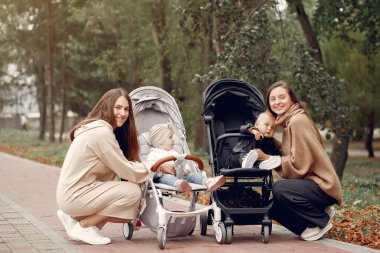 Sonbahar parkında arabalarla yürüyen iki genç anne.