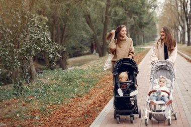 Sonbahar parkında arabalarla yürüyen iki genç anne.