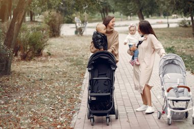 Sonbahar parkında arabalarla yürüyen iki genç anne.