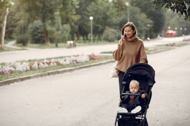 Genç anne bir sonbahar parkında faytonla yürüyor.