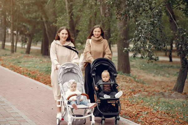 Zwei junge Mütter spazieren mit Kutschen durch einen herbstlichen Park — Stockfoto