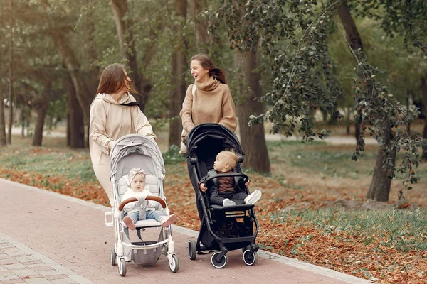 Zwei junge Mütter spazieren mit Kutschen durch einen herbstlichen Park — Stockfoto