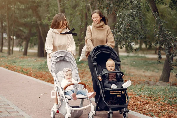 Dos madres jóvenes caminando en un parque de otoño con carruajes —  Fotos de Stock