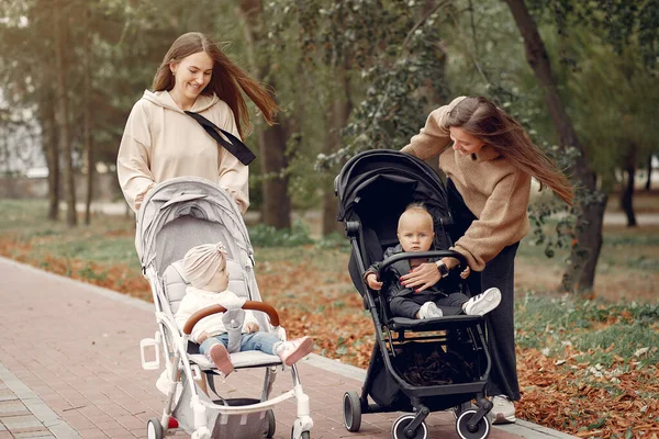 Zwei junge Mütter spazieren mit Kutschen durch einen herbstlichen Park — Stockfoto