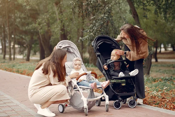 Sonbahar parkında arabalarla yürüyen iki genç anne.