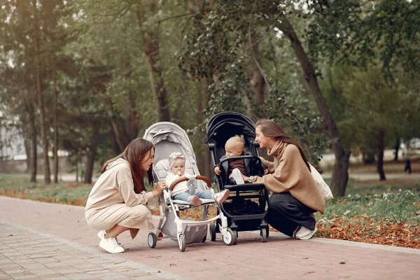 Dvě mladé matky procházející se v podzimním parku s kočáry — Stock fotografie