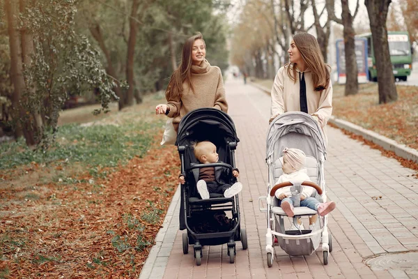 Dvě mladé matky procházející se v podzimním parku s kočáry — Stock fotografie