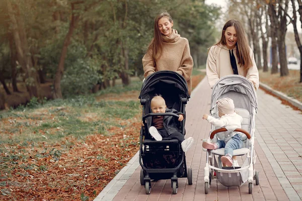 Två unga mödrar går i en höstpark med vagnar — Stockfoto