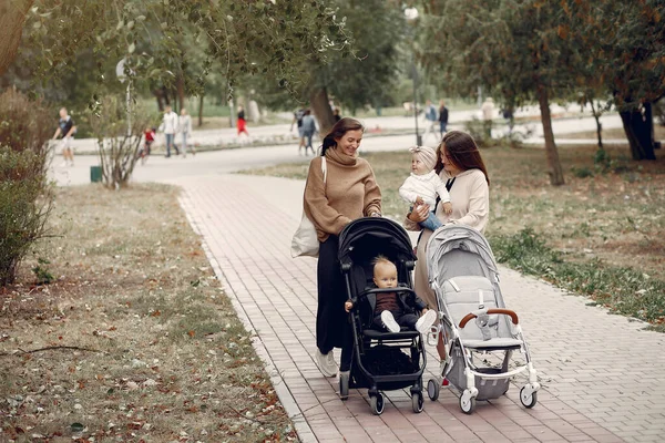 Dvě mladé matky procházející se v podzimním parku s kočáry — Stock fotografie