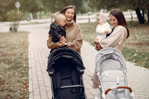 Dvě mladé matky procházející se v podzimním parku s kočáry — Stock fotografie