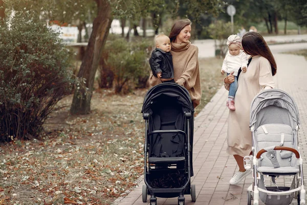 Zwei junge Mütter spazieren mit Kutschen durch einen herbstlichen Park — Stockfoto