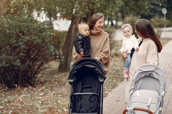 Zwei junge Mütter spazieren mit Kutschen durch einen herbstlichen Park — Stockfoto