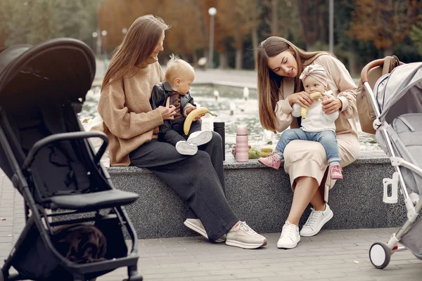 Dvě mladé matky sedící v podzimním parku s kočáry — Stock fotografie