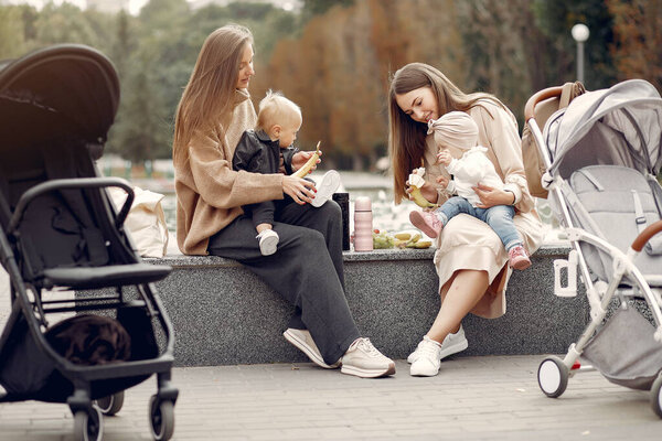 Two young mothers sitting in a autumn park with carriages