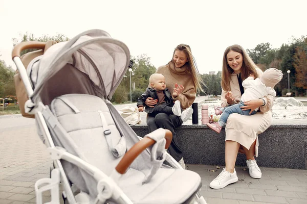 Двоє молодих матерів сидять в осінньому парку з візками — стокове фото