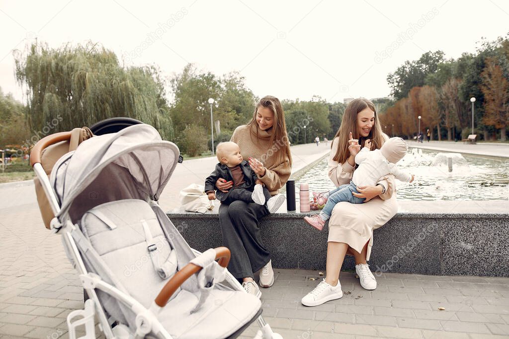 Two young mothers sitting in a autumn park with carriages