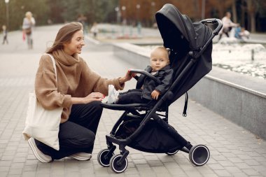 Genç anne bir sonbahar parkında faytonla yürüyor.
