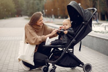 Genç anne bir sonbahar parkında faytonla yürüyor.