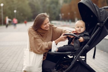 Genç anne bir sonbahar parkında faytonla yürüyor.