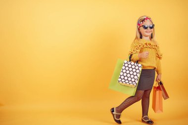 Cute little girl with shopping bags on a yellow background
