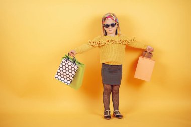 Cute little girl with shopping bags on a yellow background