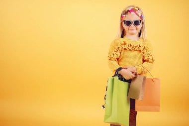 Cute little girl with shopping bags on a yellow background