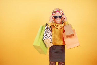 Cute little girl with shopping bags on a yellow background