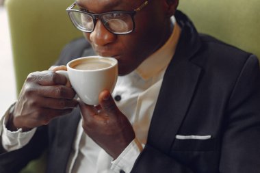 Bir kafede oturan ve kahve içen siyah bir adam.