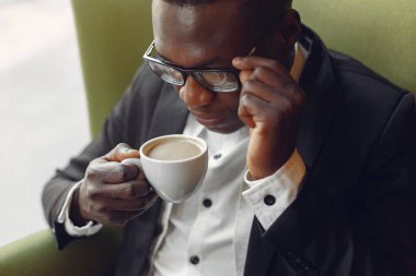 Bir kafede oturan ve kahve içen siyah bir adam.