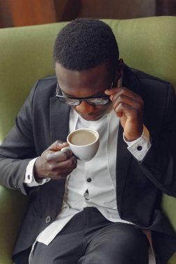 Bir kafede oturan ve kahve içen siyah bir adam.